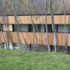 Bâtiment avec bardage en bois clair derrière des arbres