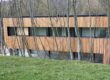 Bâtiment avec bardage en bois clair derrière des arbres