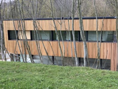 Bâtiment avec bardage en bois clair derrière des arbres