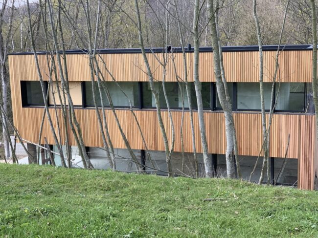 Bâtiment avec bardage en bois clair derrière des arbres