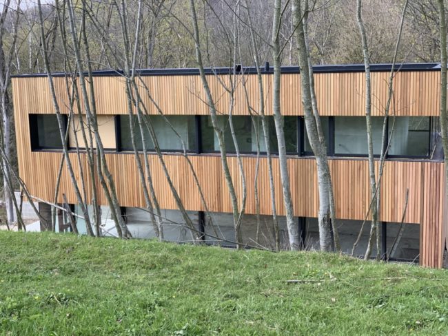 Bâtiment avec bardage en bois clair derrière des arbres