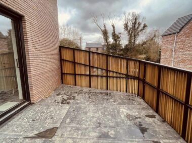 Terrasse entourée d'un bardage en bois accroché à une maison en brique rouge.