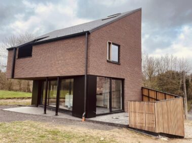Maison en brique rouge avec un bardage en bois débordant sur la droite