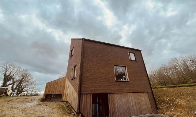Maison en brique rouge avec un bardage en bois clair débordant sur la terrasse à gauche.