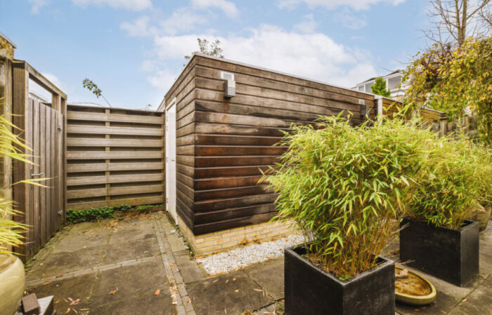 Abri de jardin moderne en bois avec toit plat, entouré de bambous et d'une clôture en bois, dans une cour bien aménagée.