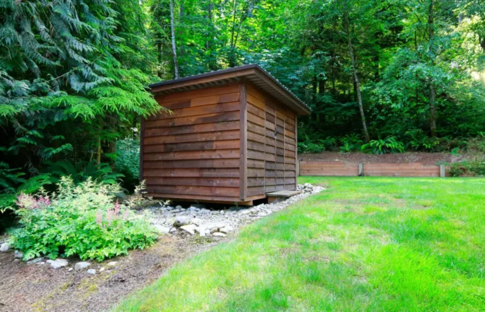 Abri de jardin à toit plat en bois dans un jardin verdoyant à l'orée des bois.