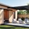 Abris de jardin en bois clair avec châssis noirs et pergola en aluminium noir avec salon de jardin annexé.