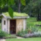 Abri de jardin en bois avec un toit naturel en pelouse, entouré de plantes, dans un parc verdoyant.