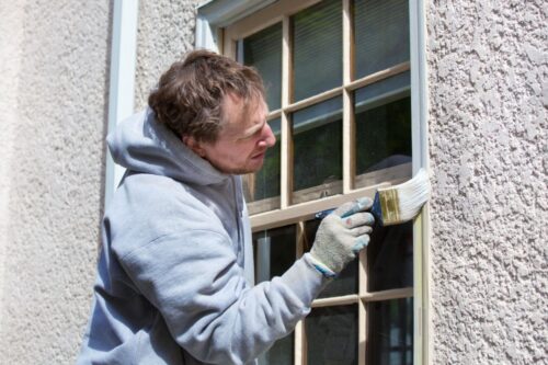 Homme en train de peindre en blanc les châssis en bois d'une maison en crépi